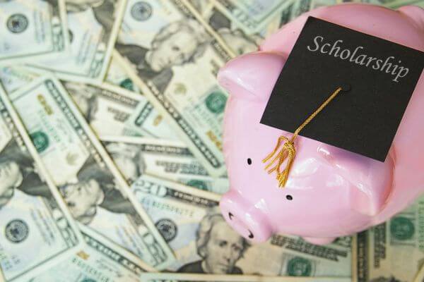 Picture of a money saving pig wearing a graduation hat saying scholarship with dollar bills in the background.