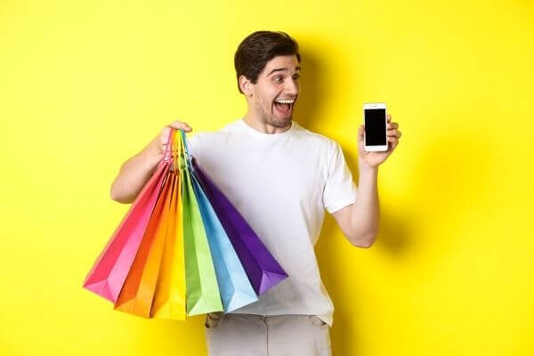 Picture of a really excited guy holding bags and his phone  to show cash bak apps really work!