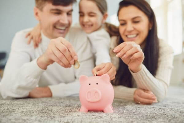 Picture of a family putting money into a savings jar with cash they have with learning how to spend less money.