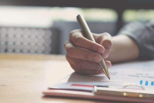 Image of a clipboard and pen in someone's hand to see can you live on $75000 per year.