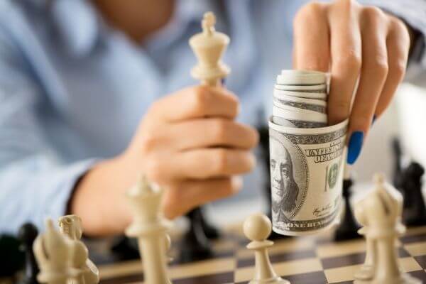 Person playing chess and showing money to say to complete a money saving challenge.