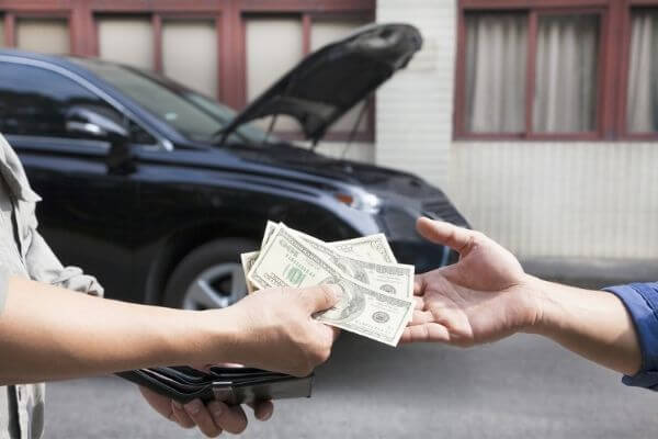 Picture of someone handing over cash with a car in the background for how your car is considered a liability.