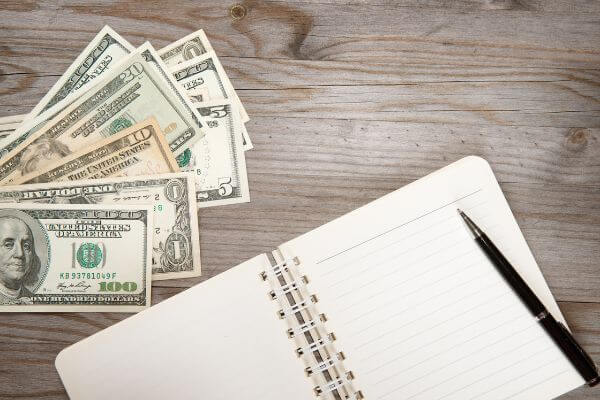 Picture of a notebook and pen with some money for things to consider when putting money to work.