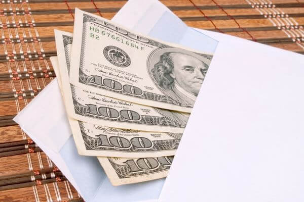 Picture of hundred dollars bills in a white envelope.