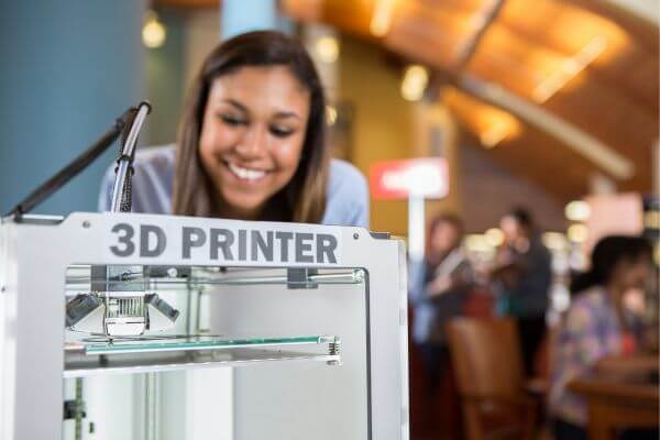 Picture of someone checking at a 3D printer at the library.