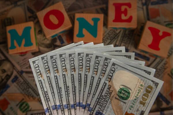 Picture of hundred dollar bills with wood blocks spelling out money.