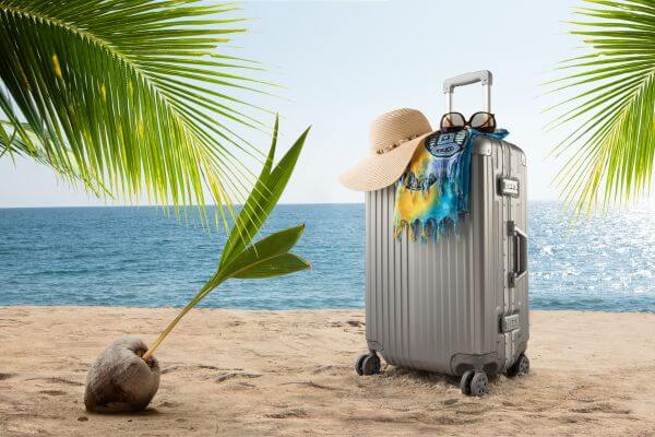 Picture of a beach with luggage sitting in the sun for what are 3 items to take on vacation.