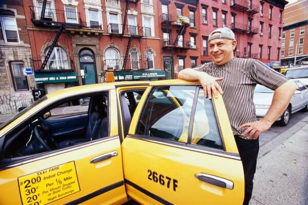 Image of a taxi driver  in a cap together in his yellow cab parking in the  street.