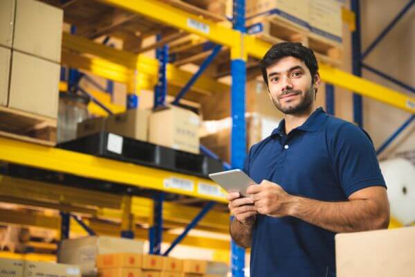 The picture of a man in a collared shirt holding a tablet and working in a warehouse.