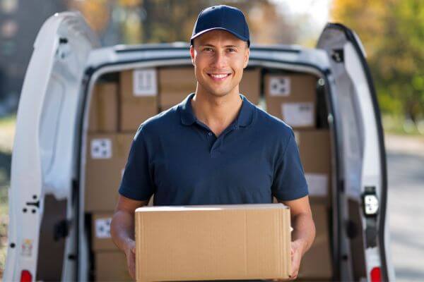 Image of a delivery man carrying a box and a car with a boxes at his back.