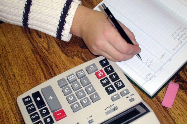 An image of a woman hand writing something in a notebook and a calculator. 