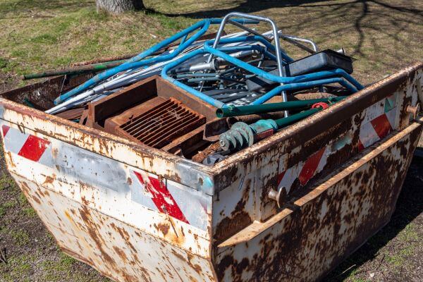 A picture of a rust metals stored in a big container as one with different old metal stuff setting aside. 