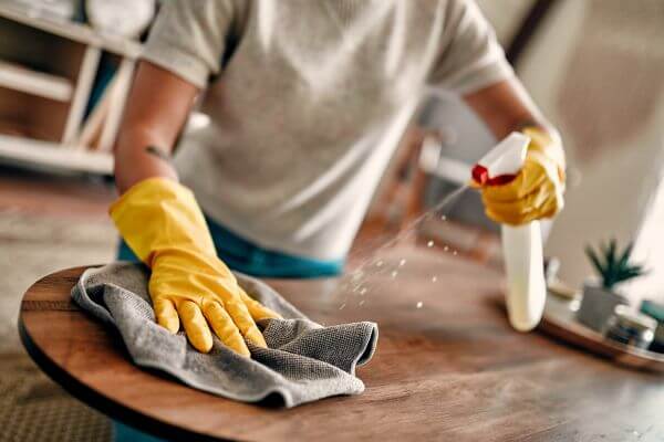 Image of the girl wearing a yellow gloves with a cleaning materials wiping the table. 