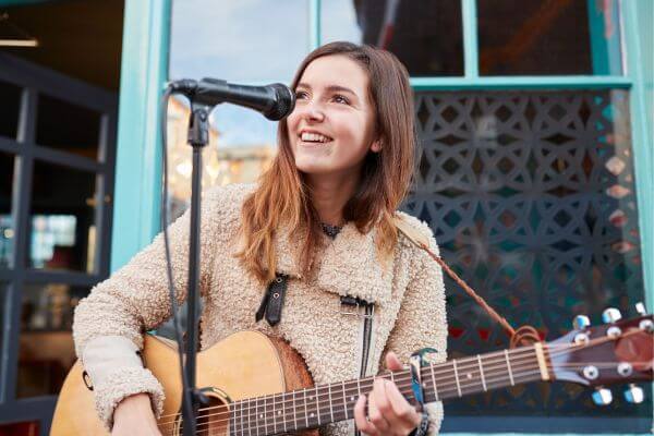 Image of the girl playing a guitar and singing with a microphone.