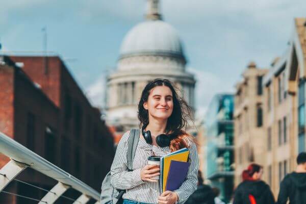 Image of a girl holding a coffee cup and notebooks while walking along the street.