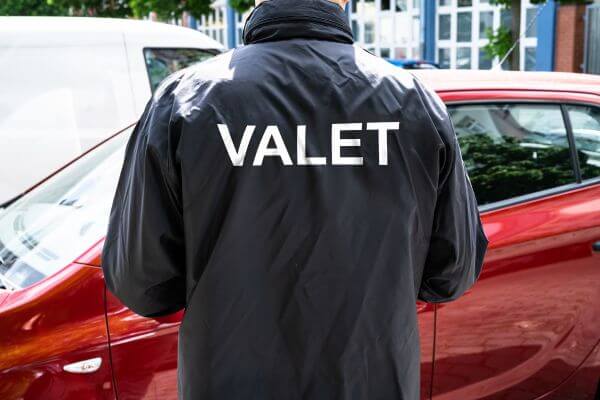 Picture of the man in a black jacket with a text of valet and a maroon car.