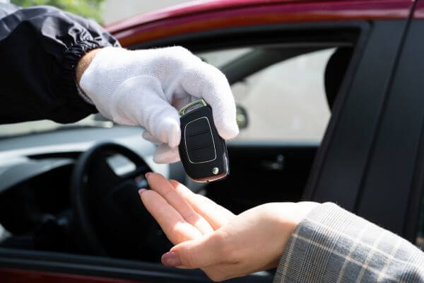 Image of the man and woman handed the maroon car key in a parking lot.