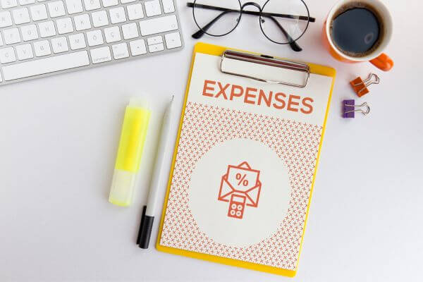 Image of the keyboard, eyeglass, coffee in a mug, pen, marker, clip, and a yellow note for expenses.