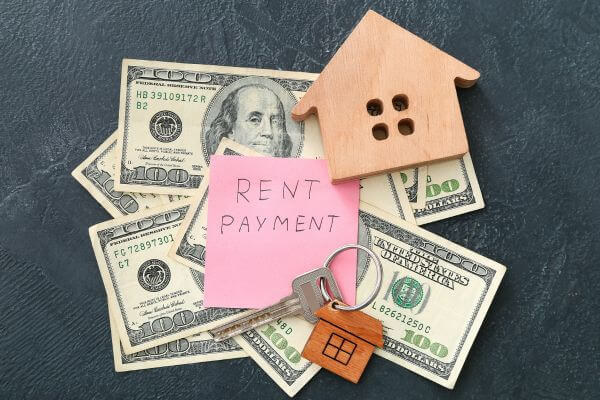 Image of the rental payment dollar bill, housing key, and a wooden-like miniature house figure.