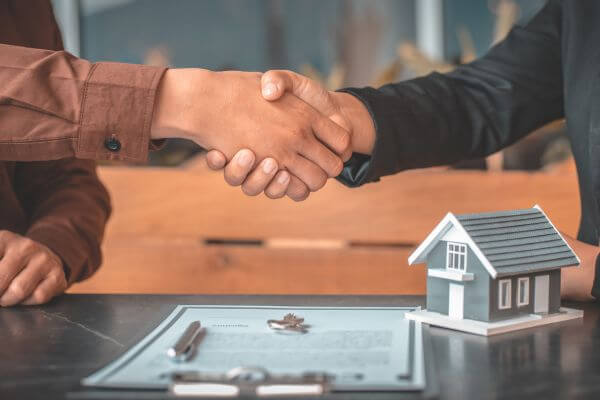 Picture of a handshake, miniature house figure, contract form, key house, and a pen.