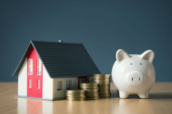 Image of a piggy bank, miniature house figure, and coins.