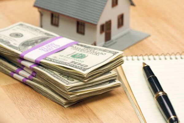 Image of the dollar bills, miniature house figure, pen, and notebook.