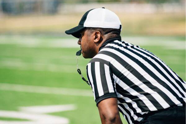 Image of a referee in a hat, black white-striped shirt, and a whistleblower.