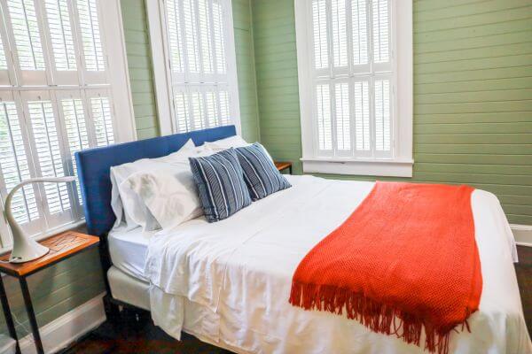 Image of a space room with a bed, pillows, comfortable blanket, small table, and light.