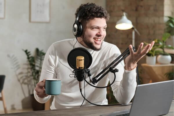 Image of the man wearing headphone and carrying a cup of coffee doing a podcast.