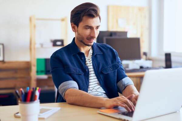 Image of a man navigating his gray laptop along his desk.