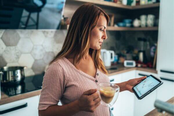 Picture of the mom carrying a cup of coffee while checking something on her tablet. 