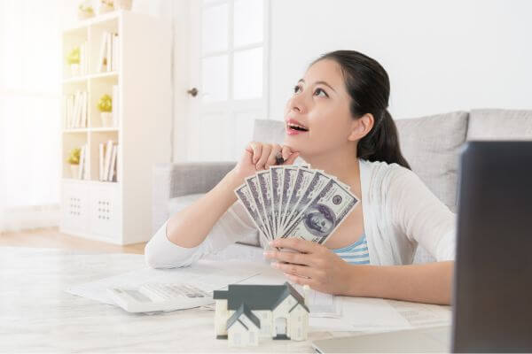 Image of a woman holding a dollar bill,  together with  her stuffs around while thinking an idea.