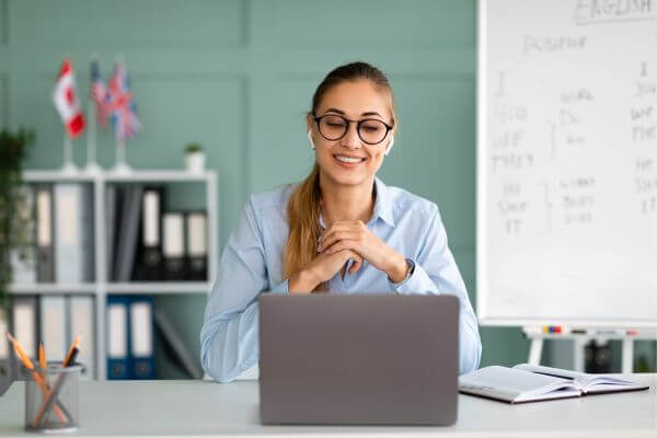 Image of a woman wearing an eyeglasses and earpads while looking at the laptop and smiling.