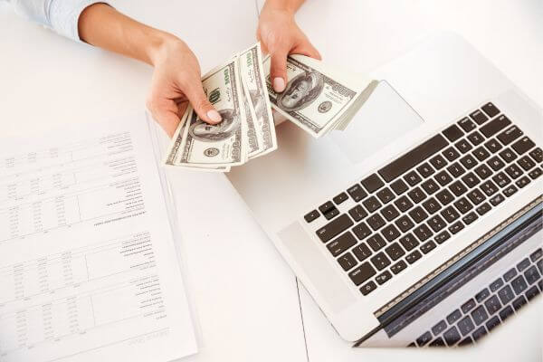 Image of a woman counting money together with her laptop and papers on the desk.