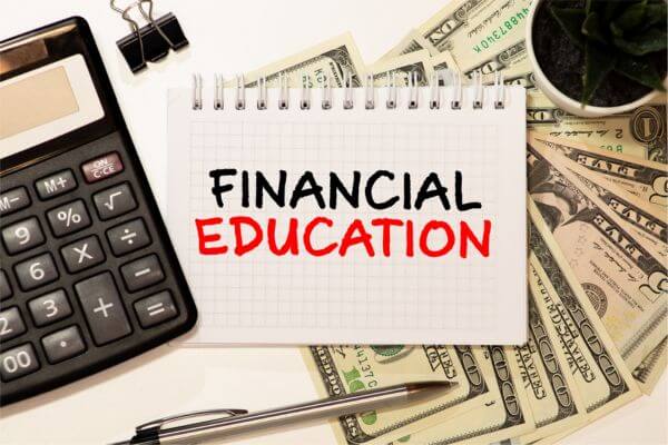Image of calculator, dollar bills, pen, and a white paper defining to become educated in financial issues and be guided to achieve financial freedom.