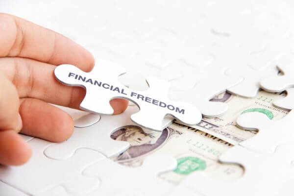 Picture of the hand, dollar bill, and a puzzle developing the financial freedom piece.