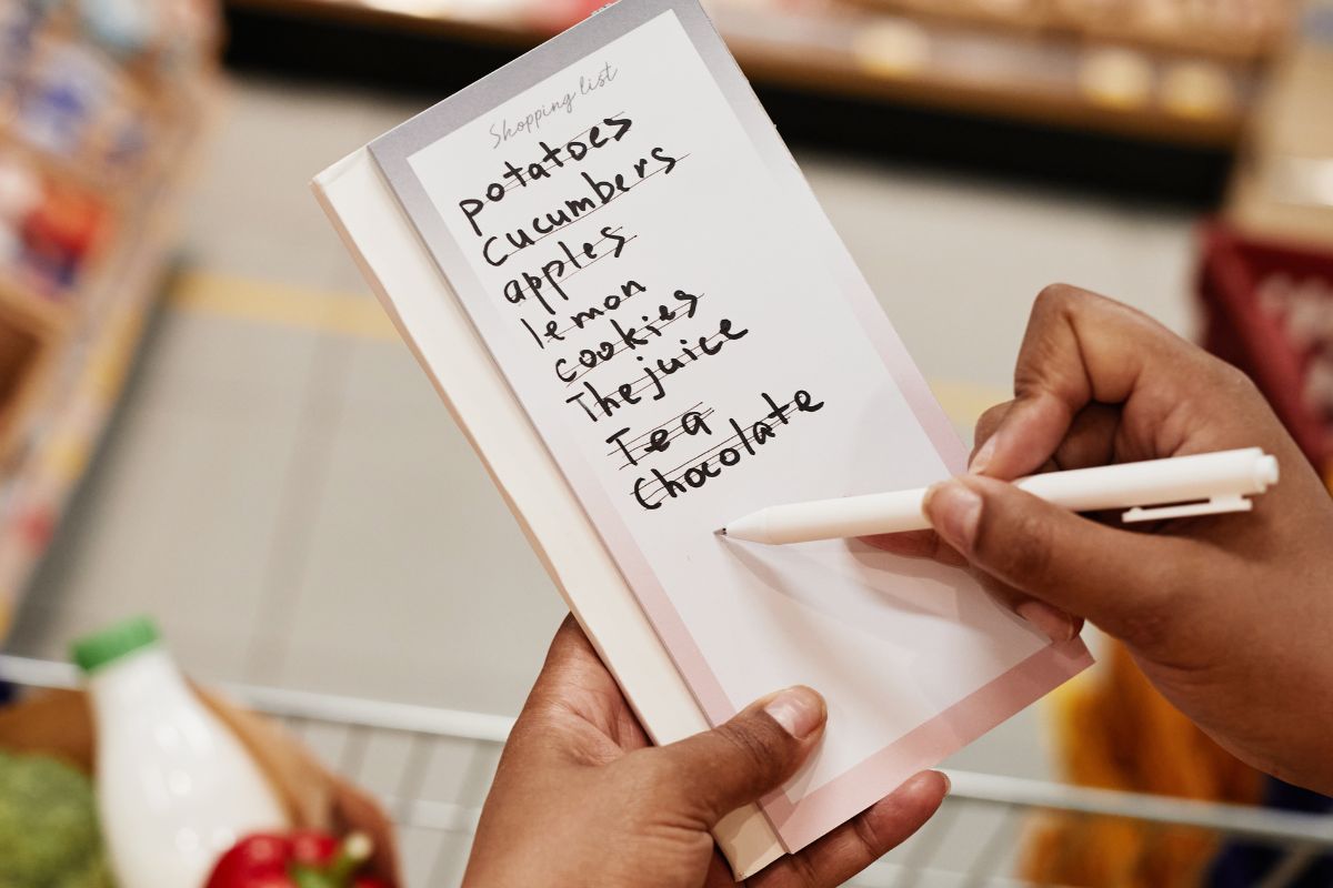 Picture of a lady's hand making a grocery list. 
