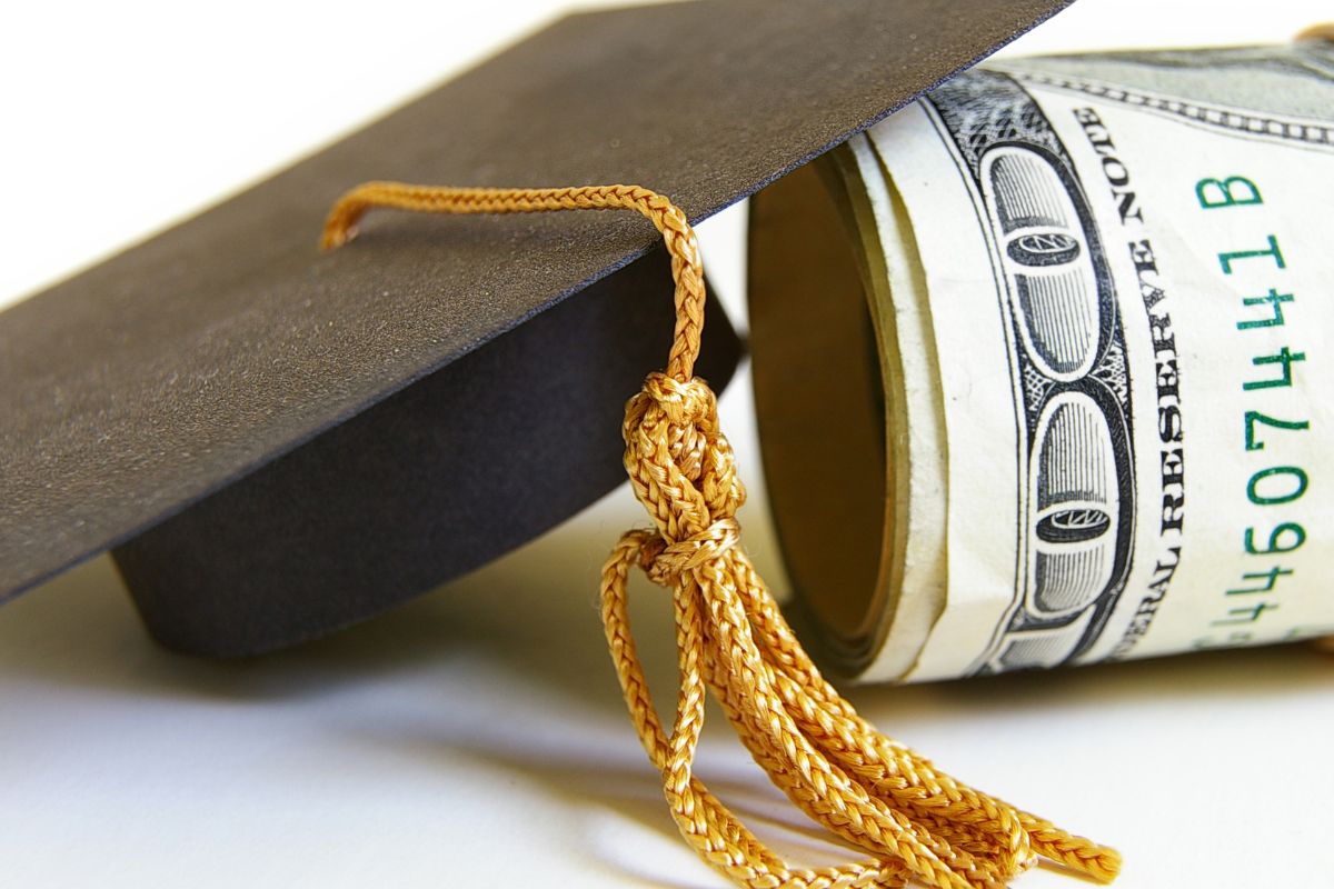 Picture of a roll of hundred dollar bills and a graduation cap.