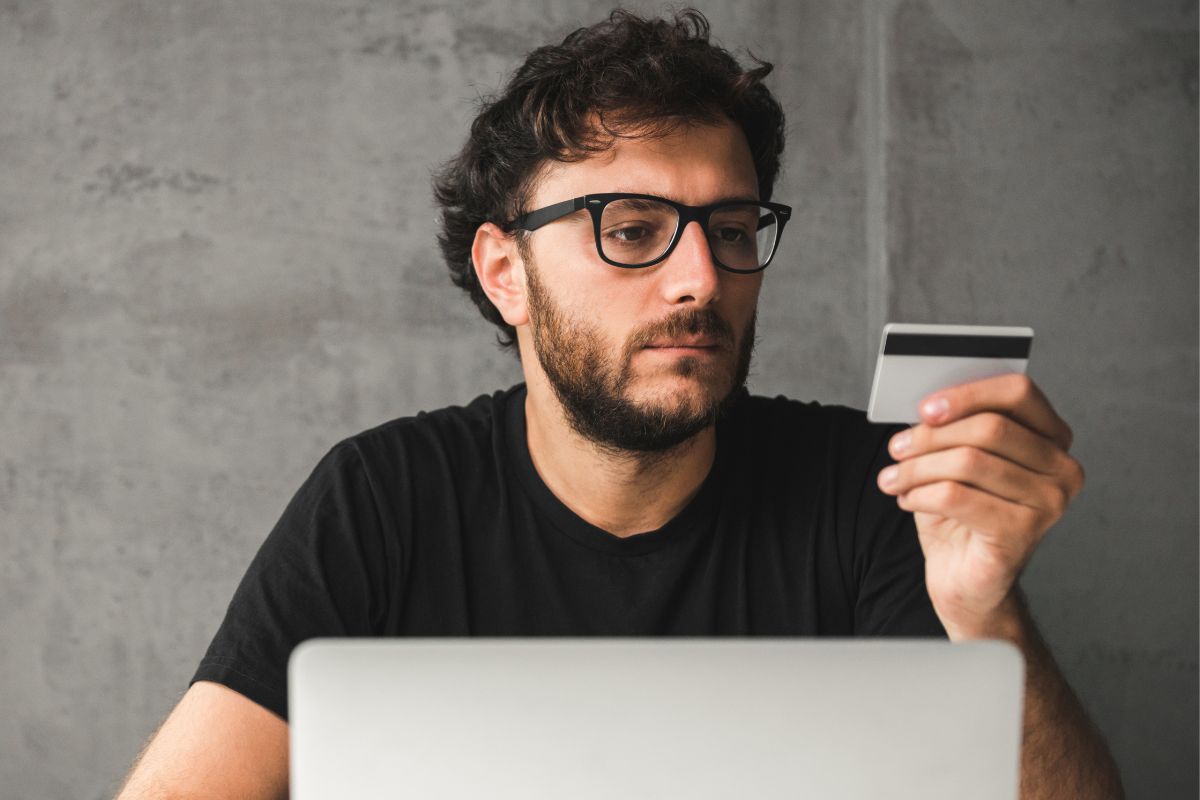 Picture of a man looking at a credit card and laptop.