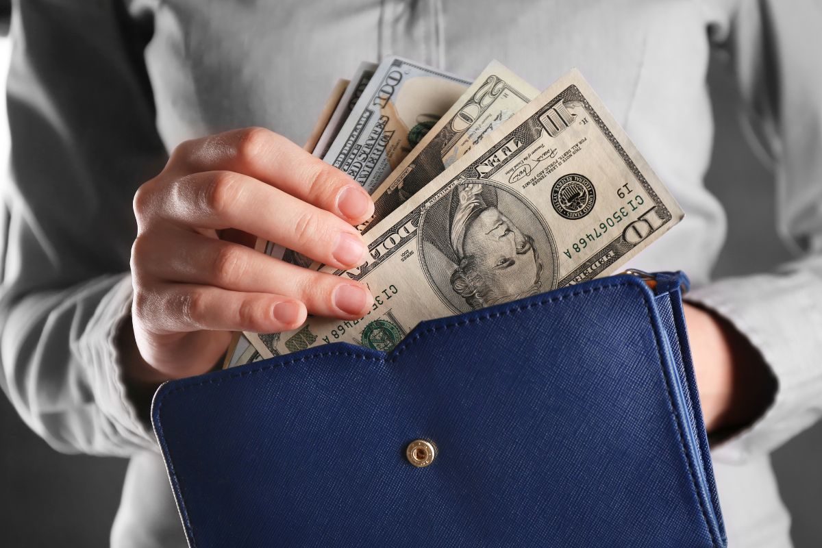 A woman's hand putting her money in her wallet.