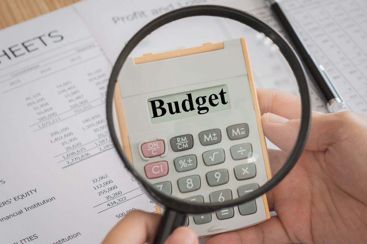 A man's hand holding a calculator with budget wording.