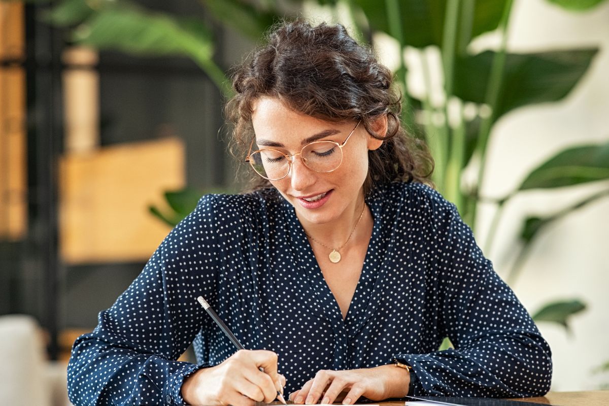 The image shows a woman writing on a piece of paper.