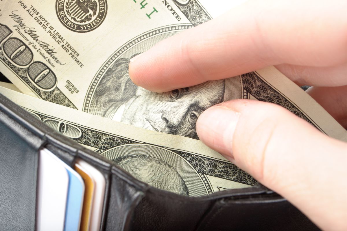 A mão de uma mulher colocando seu dinheiro em sua carteira.