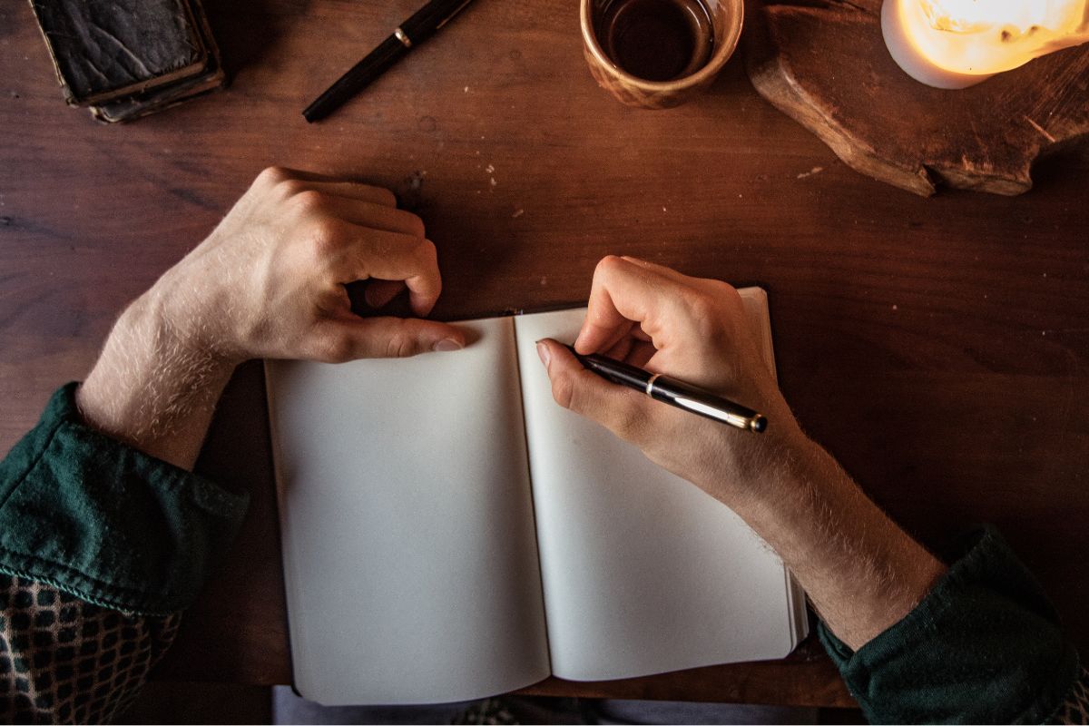 The photo shows a man's hand and writing on a notebook.