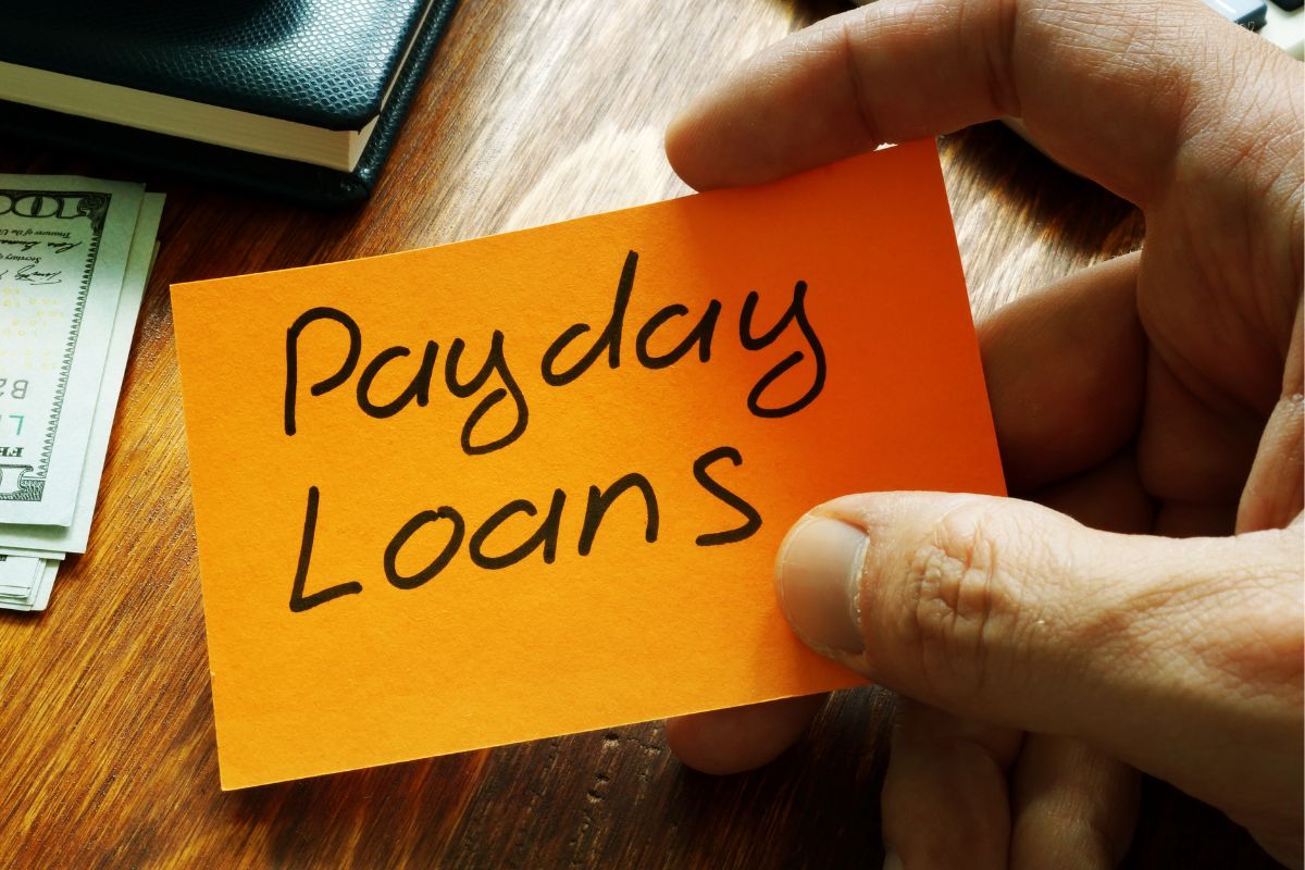 A man's hand holding a paper with payday loans wording.