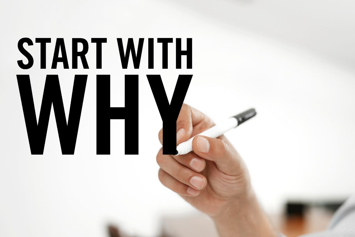A man's hand is writing a start with why.