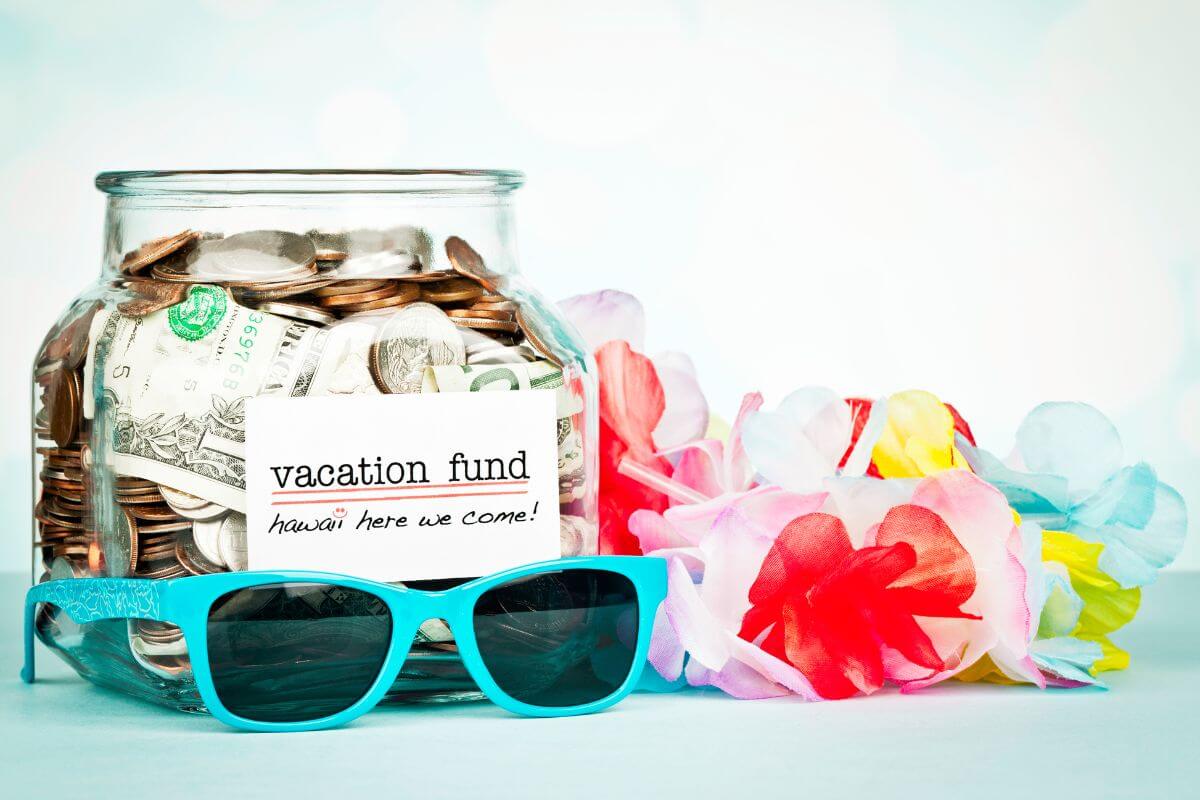 The photo of eyeglasses, crepe paper flower type, and a jar filled with dollar bills and coins refer to a vacation fund that lets you save money for trips without dipping into regular savings.