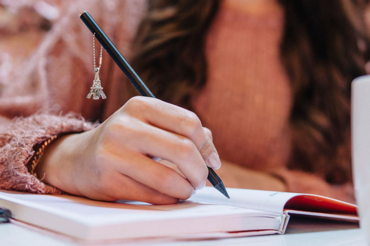 The photo shows a woman writing in a notebook.