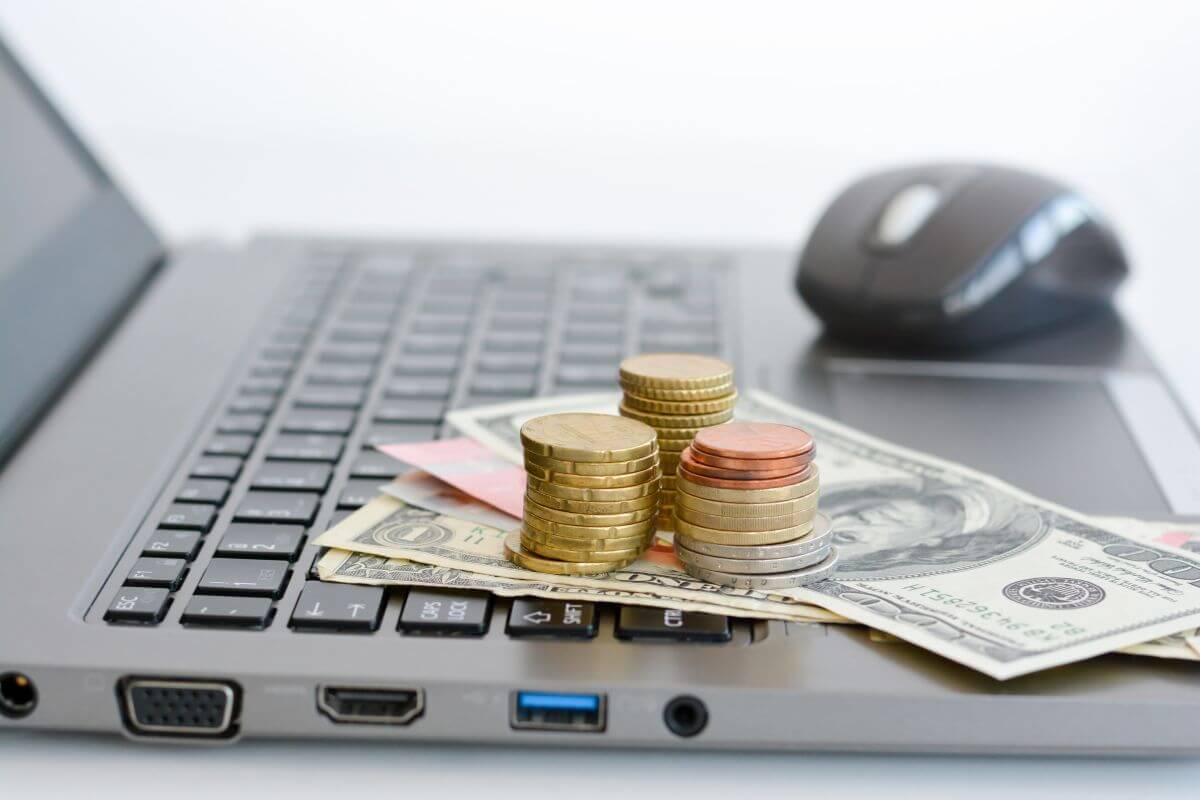 The image tells about a mouse, laptop, dollar bills, and coins indicating to look for ways to make money online to boost your income.
