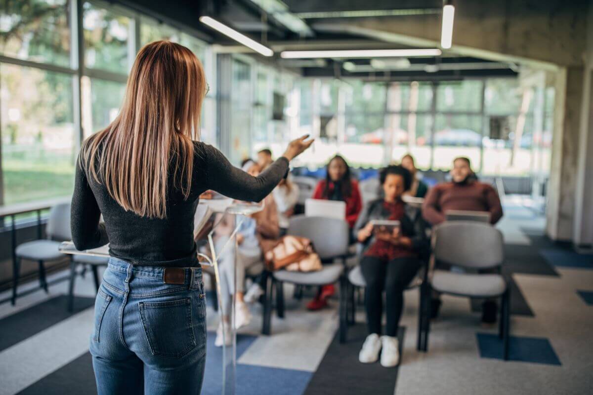 The image tells about the coach and her audience sharing her expertise to help achieve their goals and one of the most profitable careers.